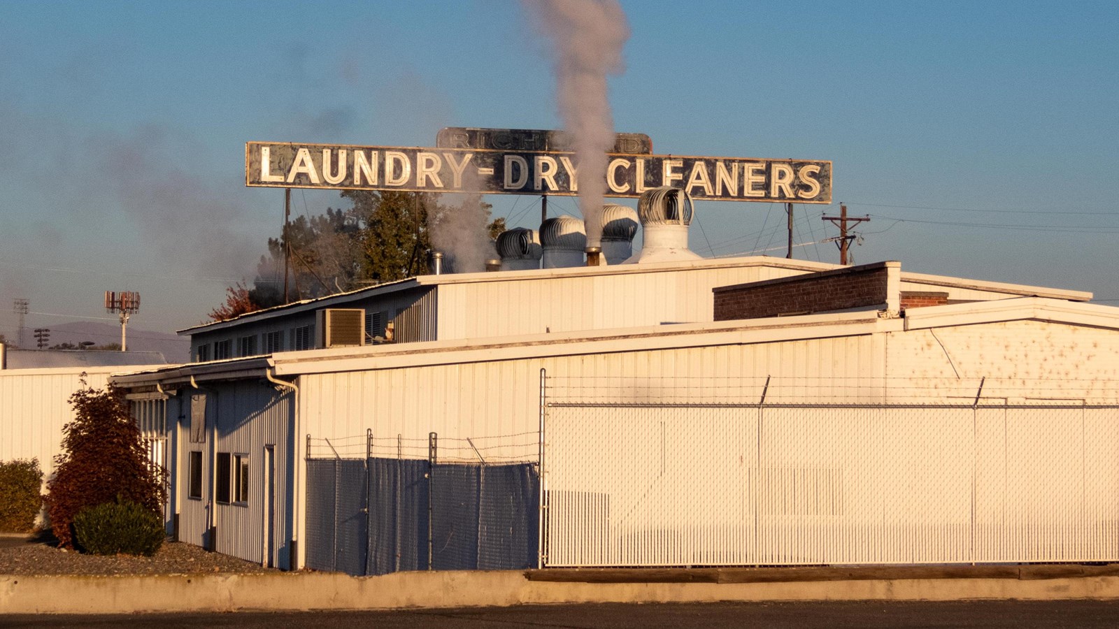 Color photograph of a medium-sized industrial building with smoke rising from multiple vents