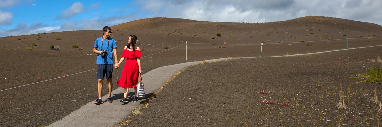 Two people holding hands on a paved path through a cinder-covered landscape