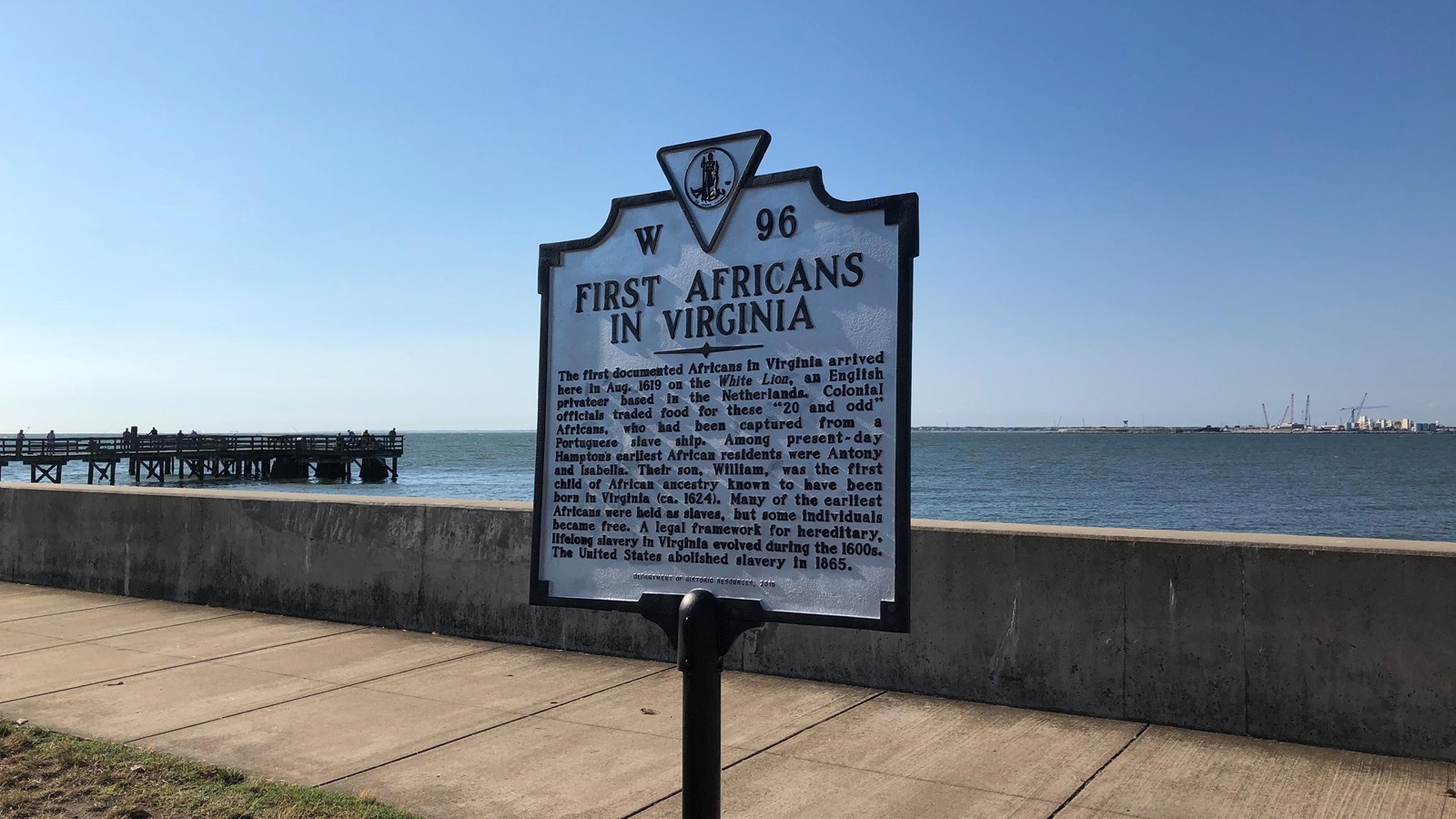 A historical marker sign on a seawall notes the arrival of the first Africans in Virginia.