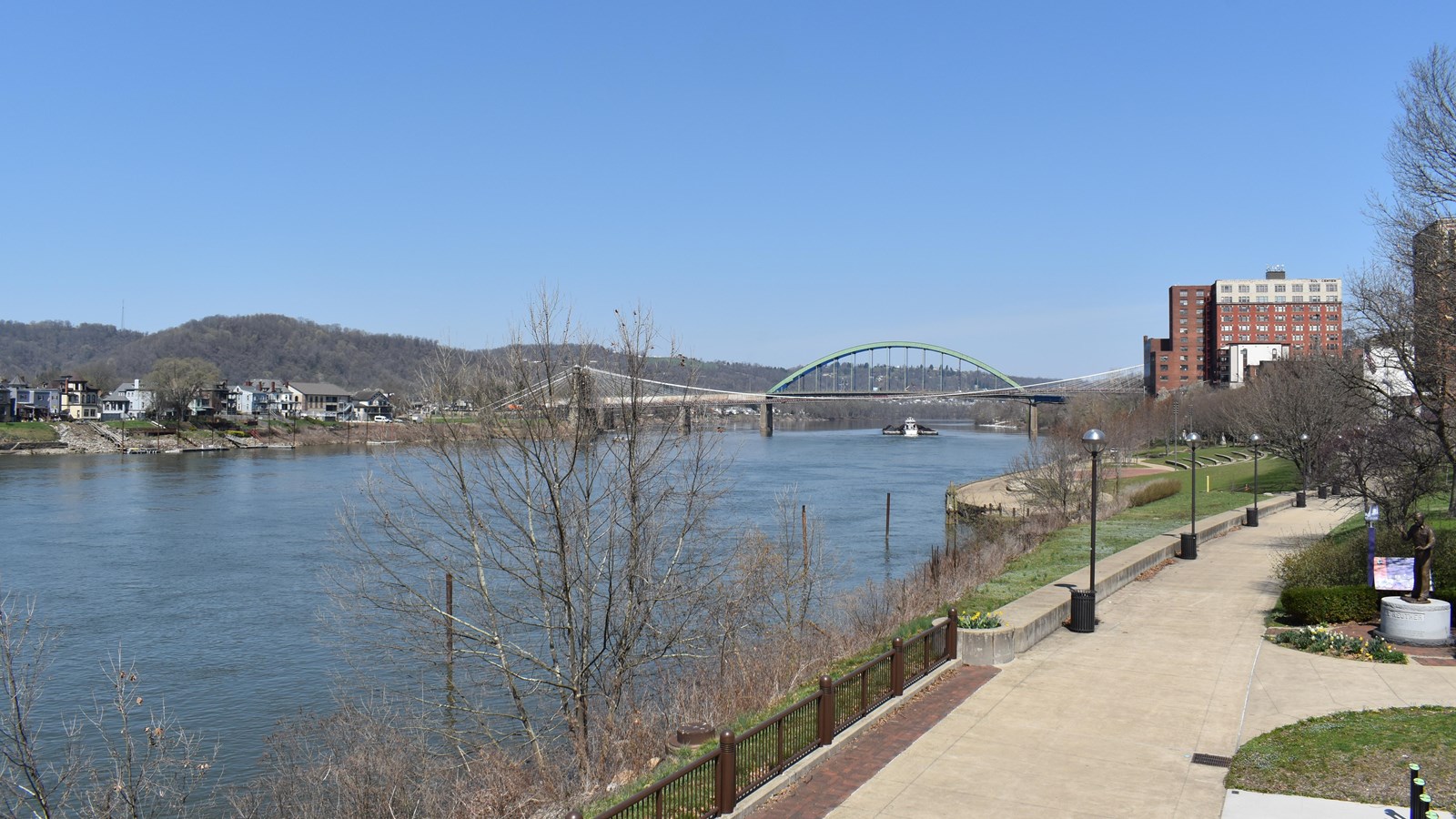 This photo shows a scenic riverside view of the Ohio River at Wheeling, West Virginia. A wide, paved
