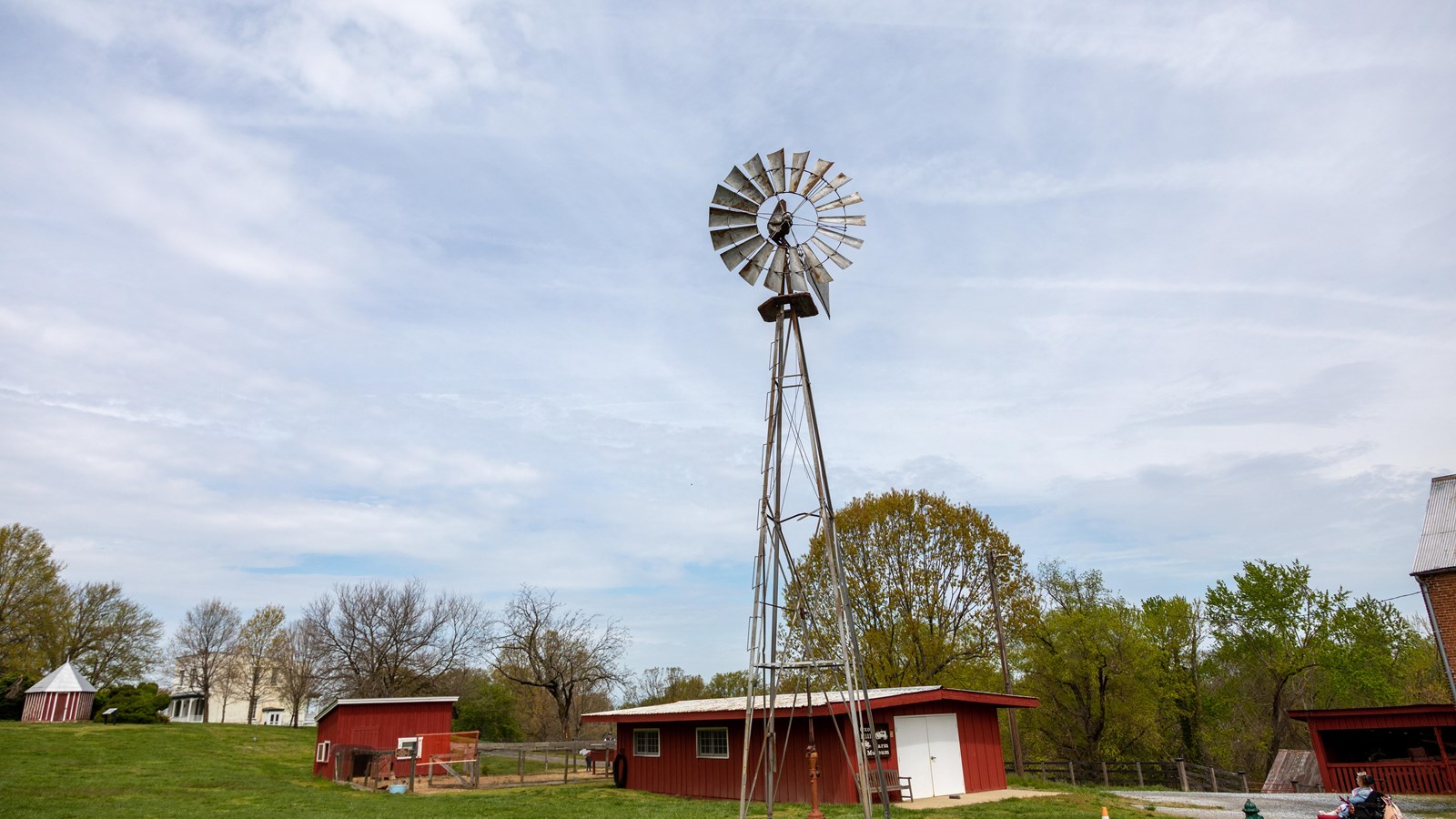 A silver windmill stands tall against a blue sky with red farm buildings scattered around it