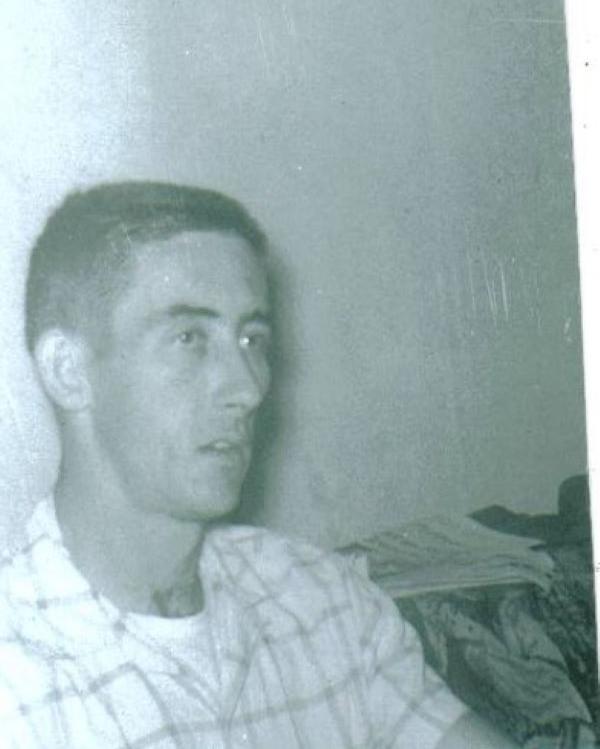 Man with short hair and a button up shirt sitting on couch.