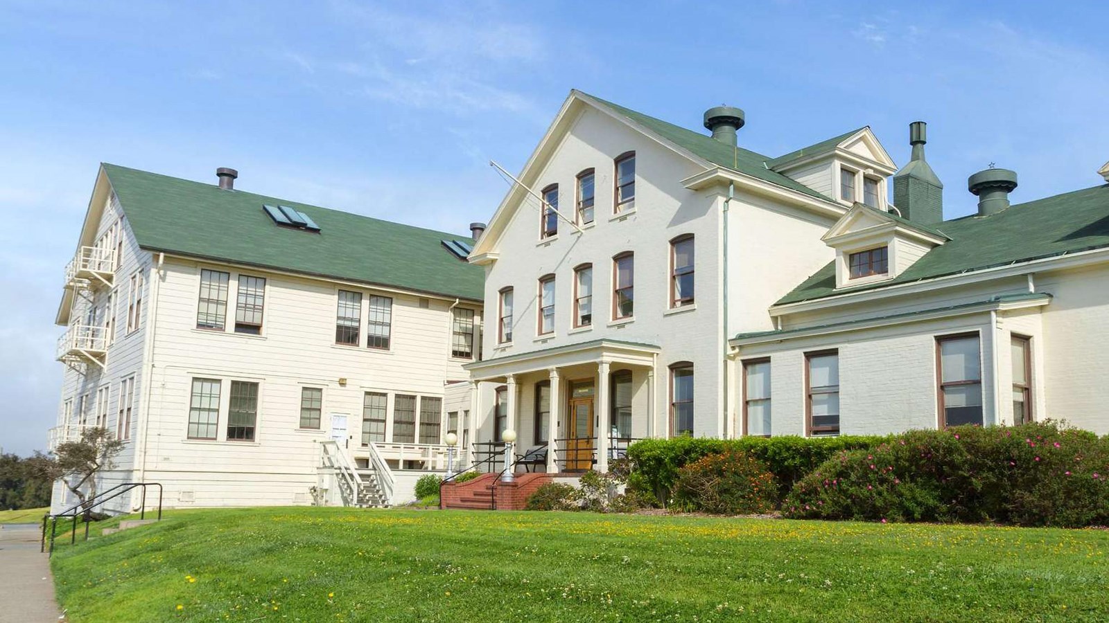 A wide green lawn in front of the white wood three story structure with green roof.