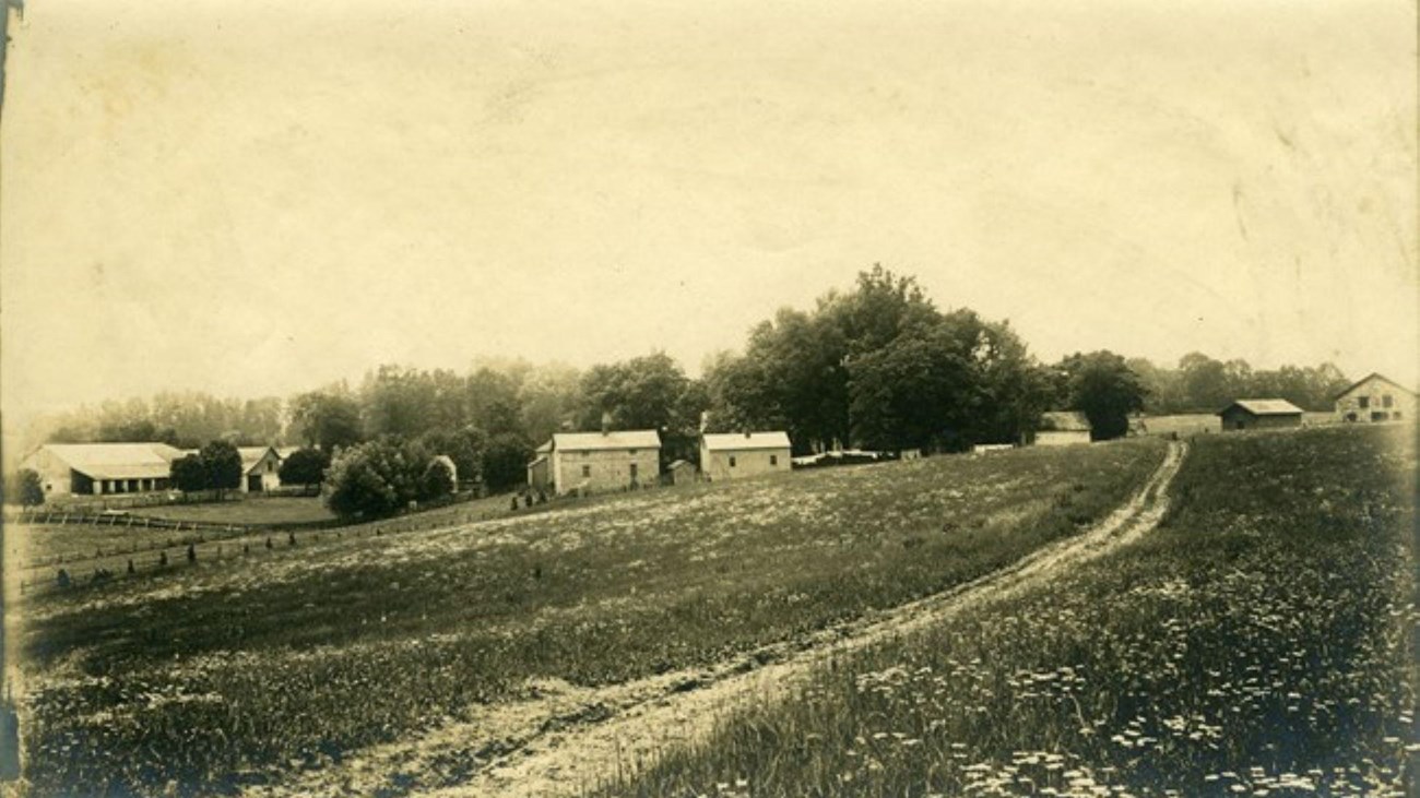 A black and white historic photograph of the farm side structures.