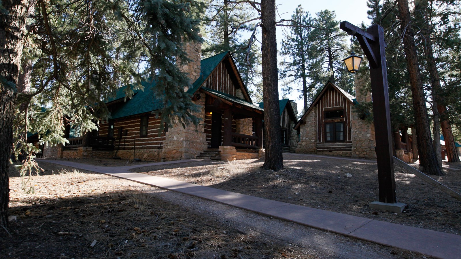 Two rustic style log cabins with stone foundations and green roofs along a sidewalk