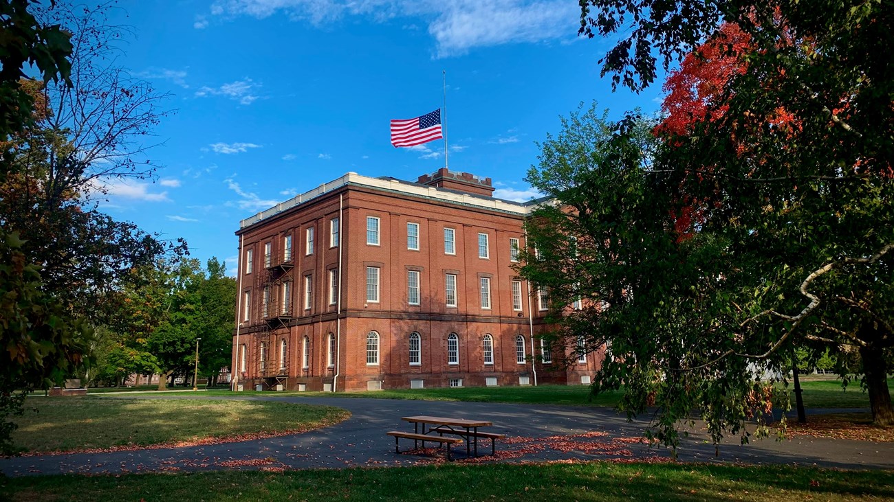 Springfield Armory, with the flag at half staff, with a path and a picnic table visible. 