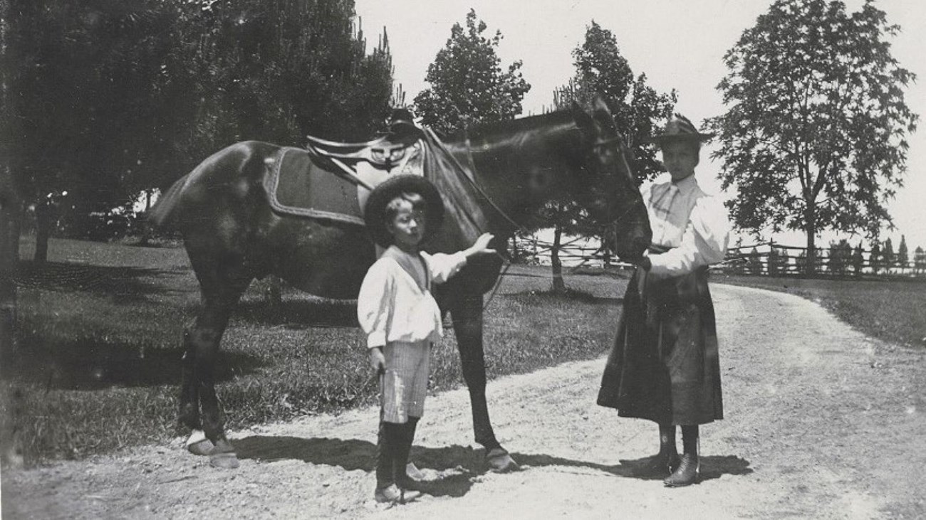 A young Ted Jr stands next to a horse led by his older sister Alice on the grounds of Sagamore Hill.