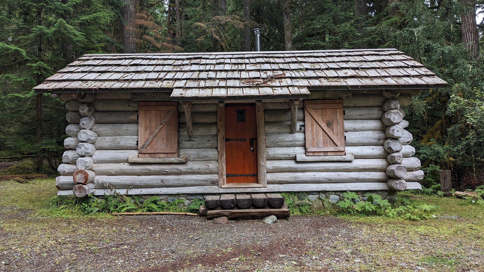 Log frame, one room, one story rectangular cabin with a medium-pitched cedar shake gable roof 