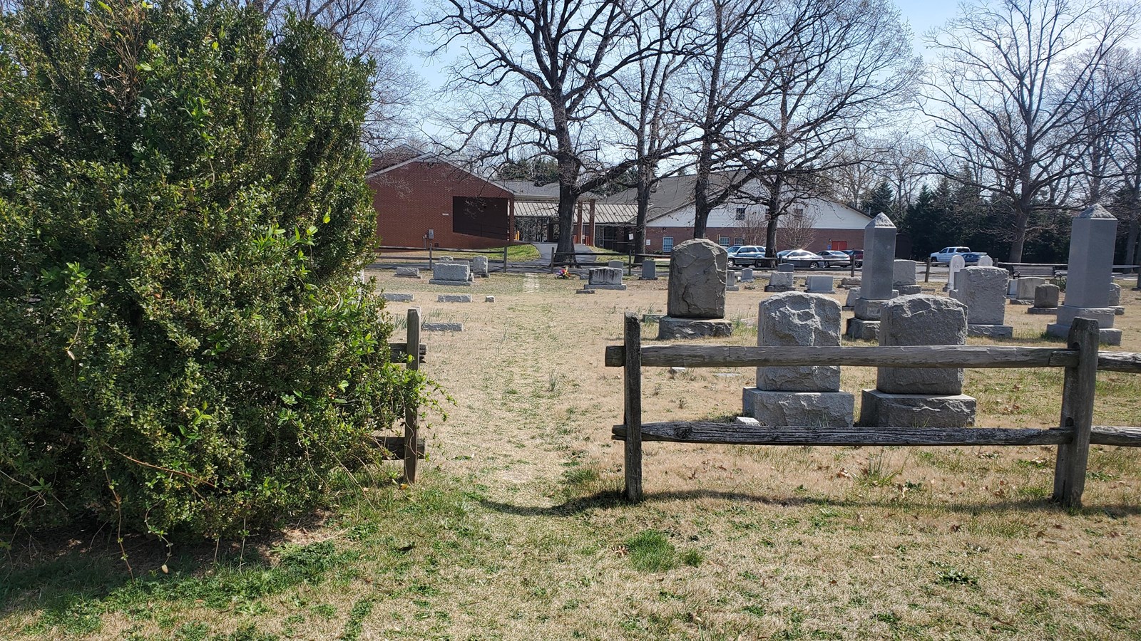 An opening in a wooden fence that leads to a church cemetery.