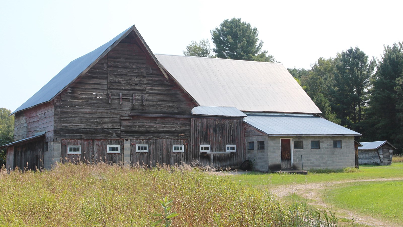  A dirt driveway leads to a tall, faded barn. the right, a stone addition drawing attention. 