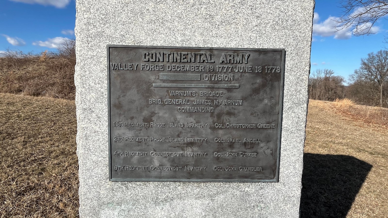 A photograph of a large granite block monument with a rectangular bronze plaque mounted to the front