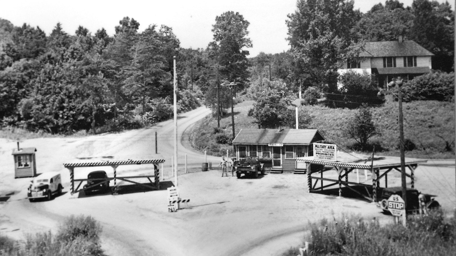 A black and white photo of a guard post with a two-story farmhouse on a wooded hill above.
