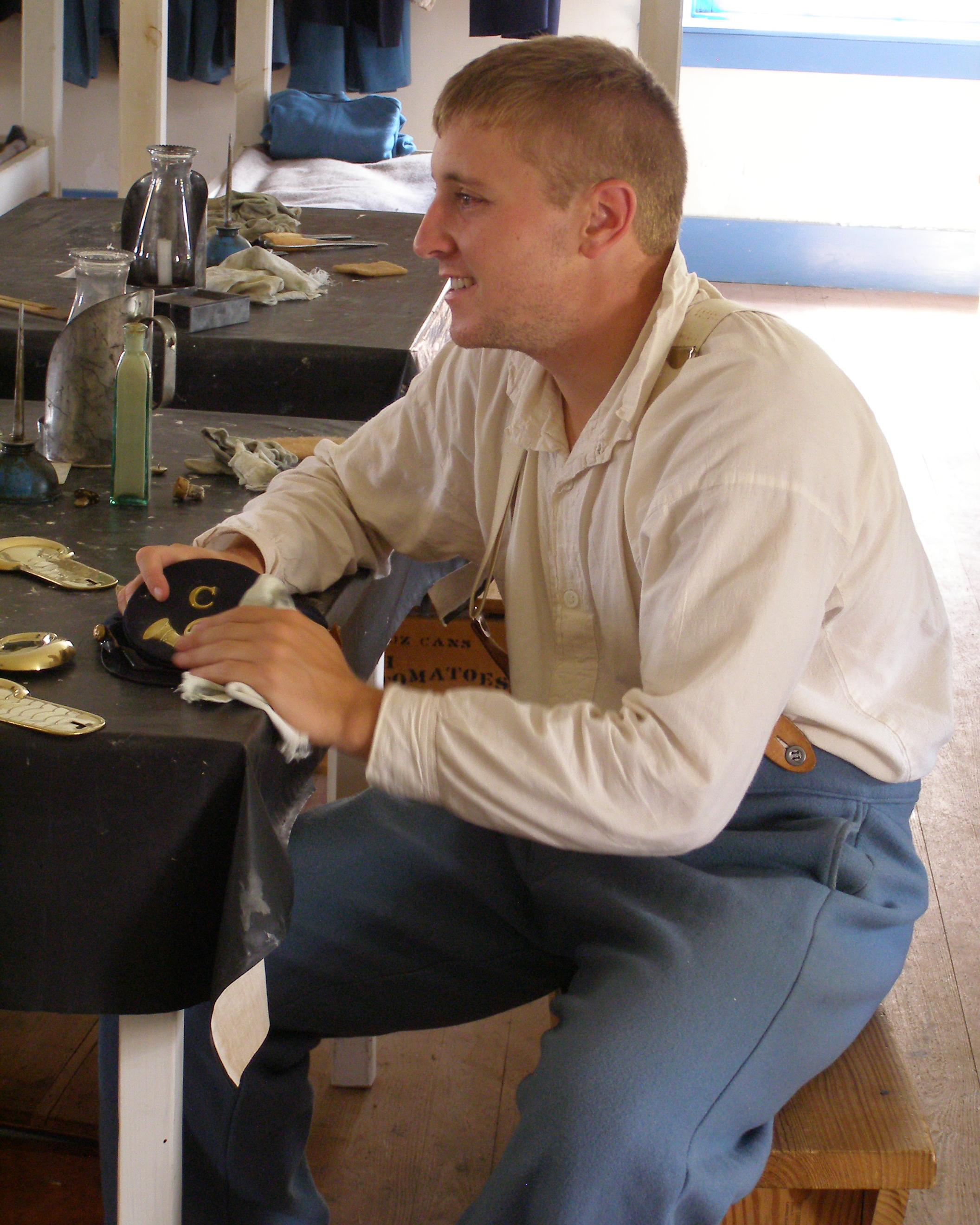 Young man in 19th century US army uniform polishing brass in the barracks.