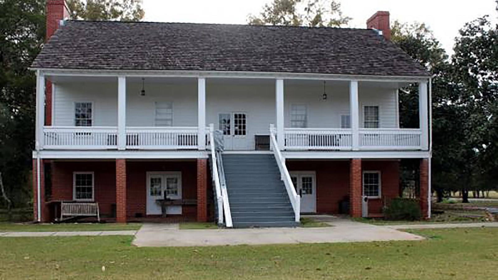 A historic two-story home with a large veranda and leading staircase.