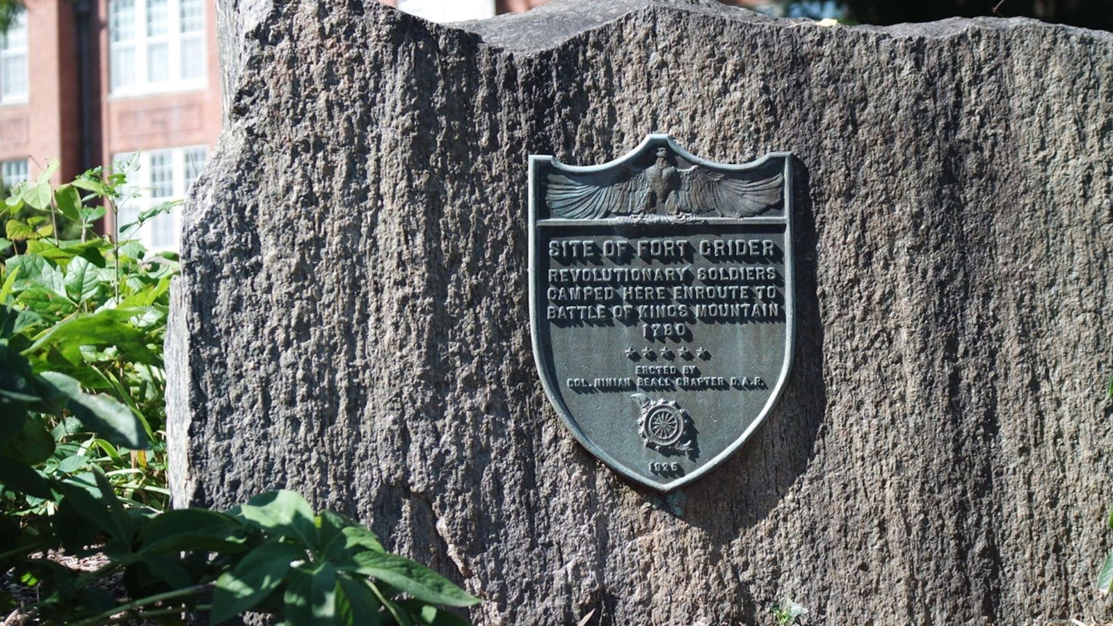 A plaque is on a rock in front of a large brick building.
