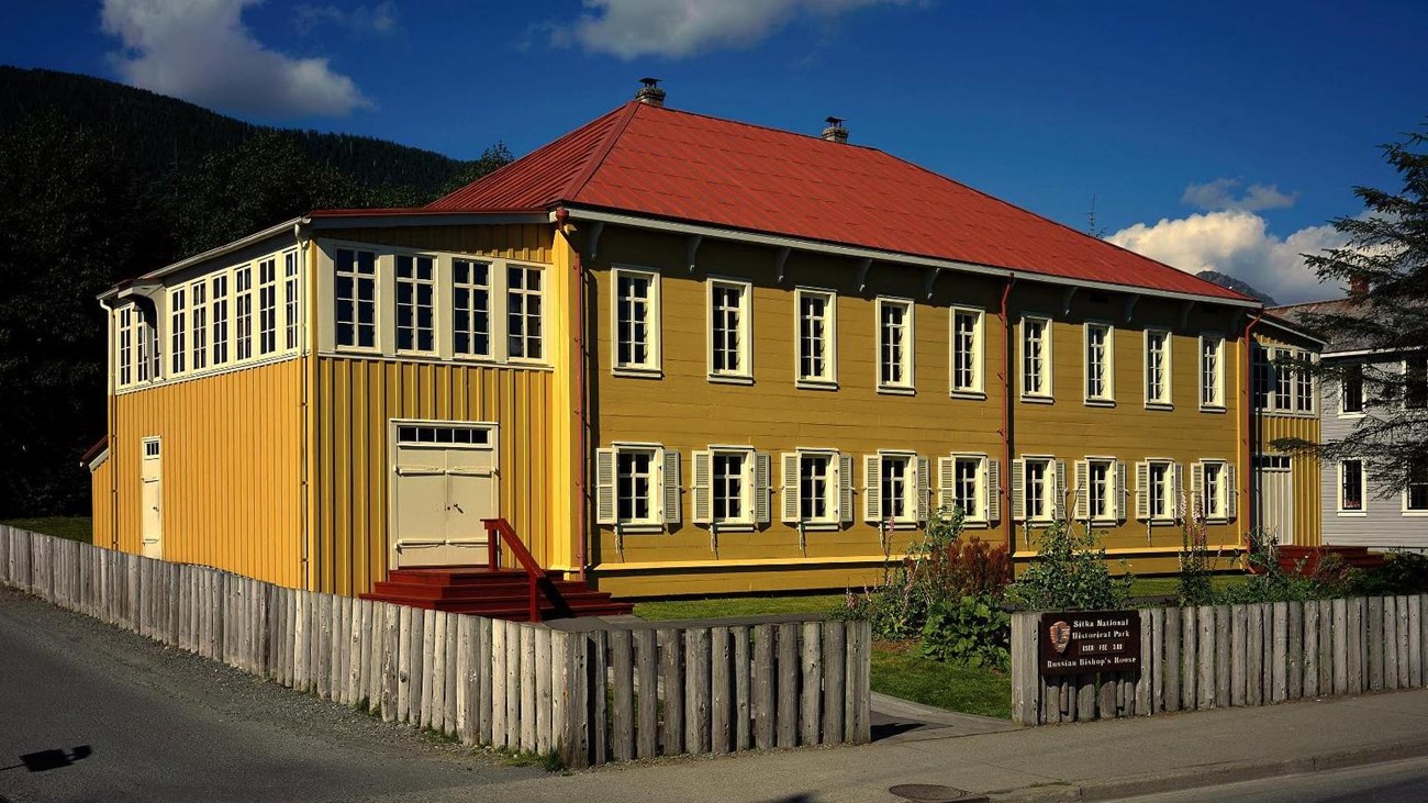 Two-story historic building with yellow walls and red metal roof.