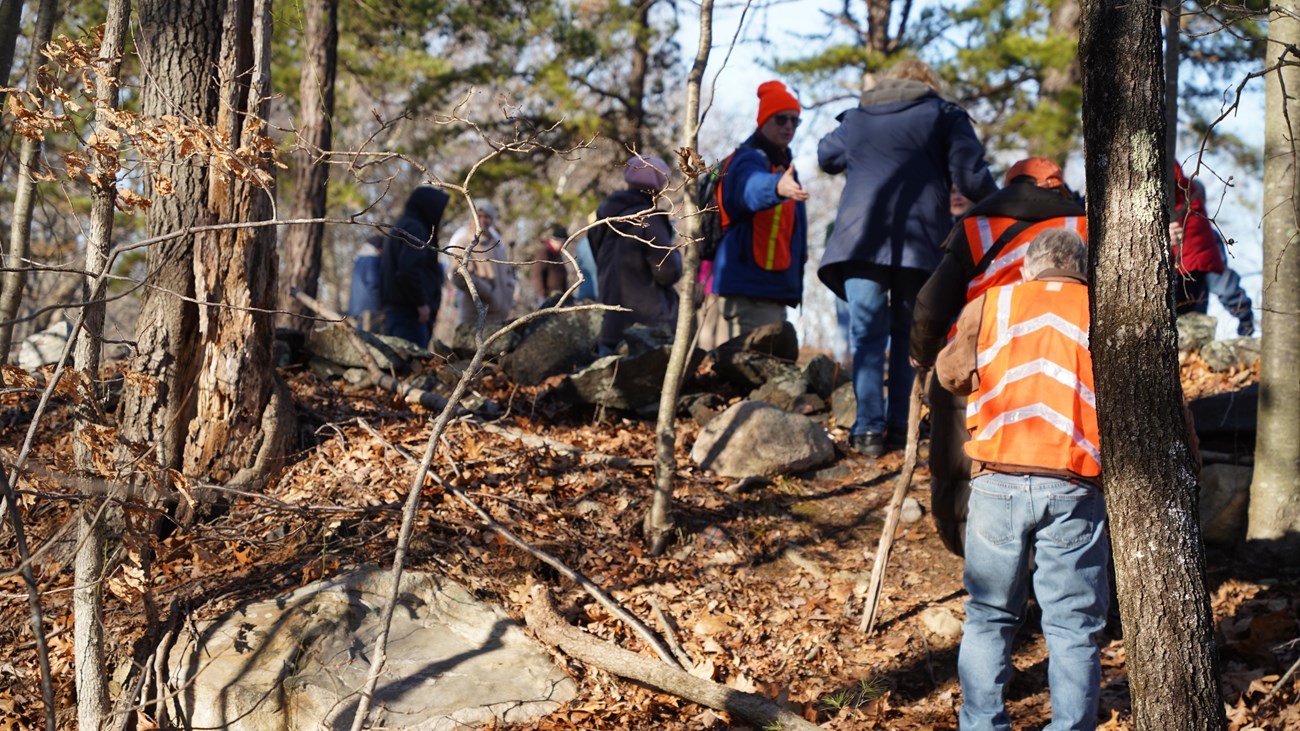 People walking up hill. Some wearing orange safety vests