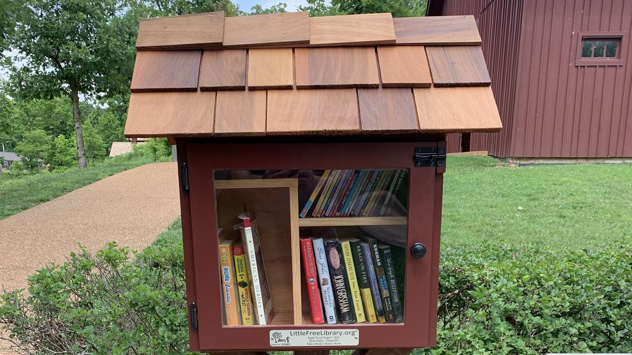 Collection of books inside red wooden box with cedar shingle roof. 