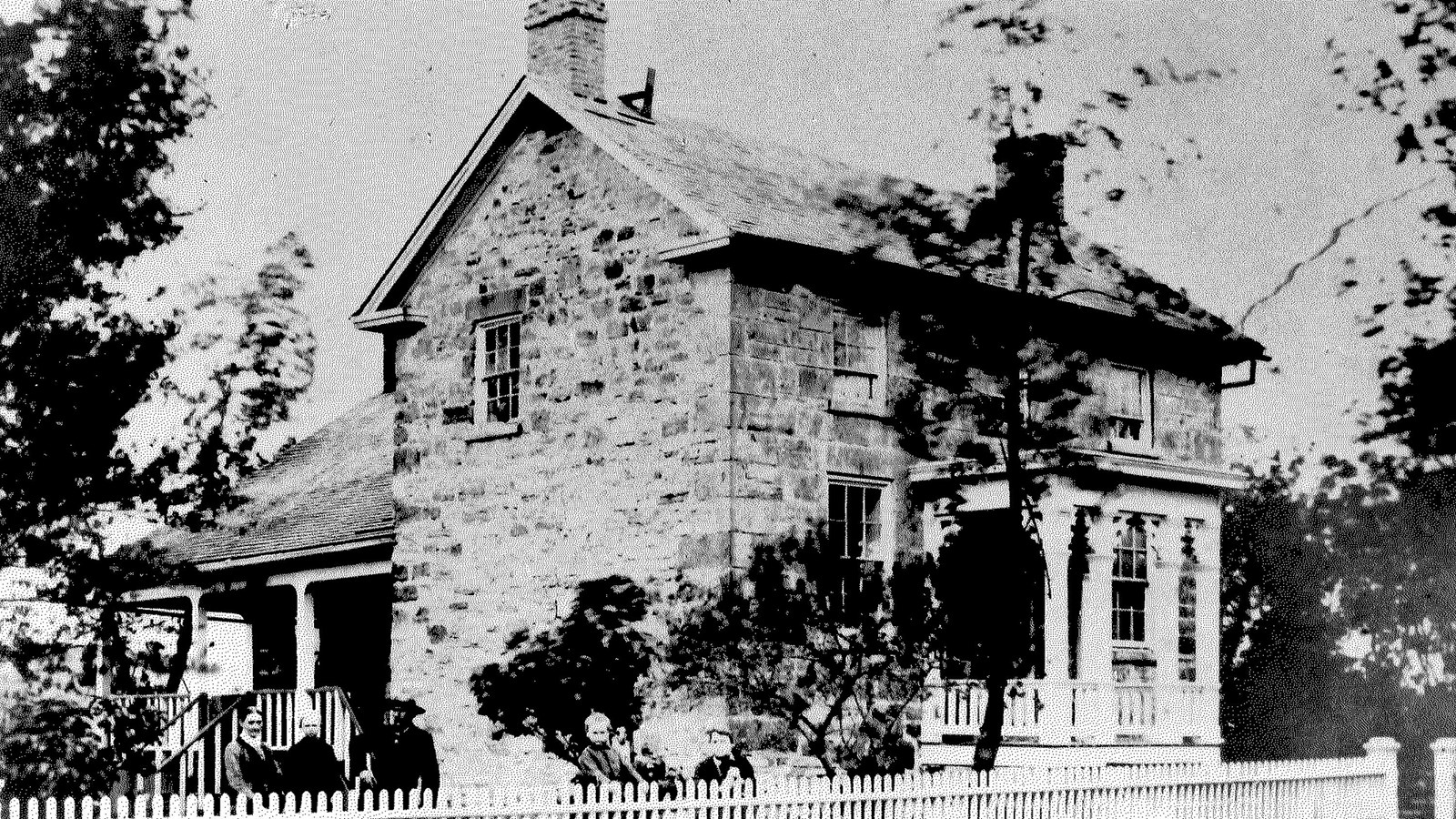  two-story stone house. Wooden steps lead up to a covered porch in front of the central door.