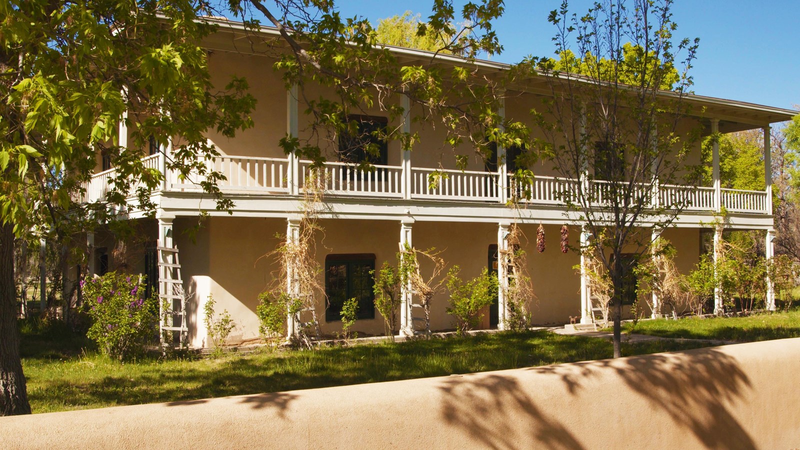 Two story light tan adobe building with full wraparound porch.