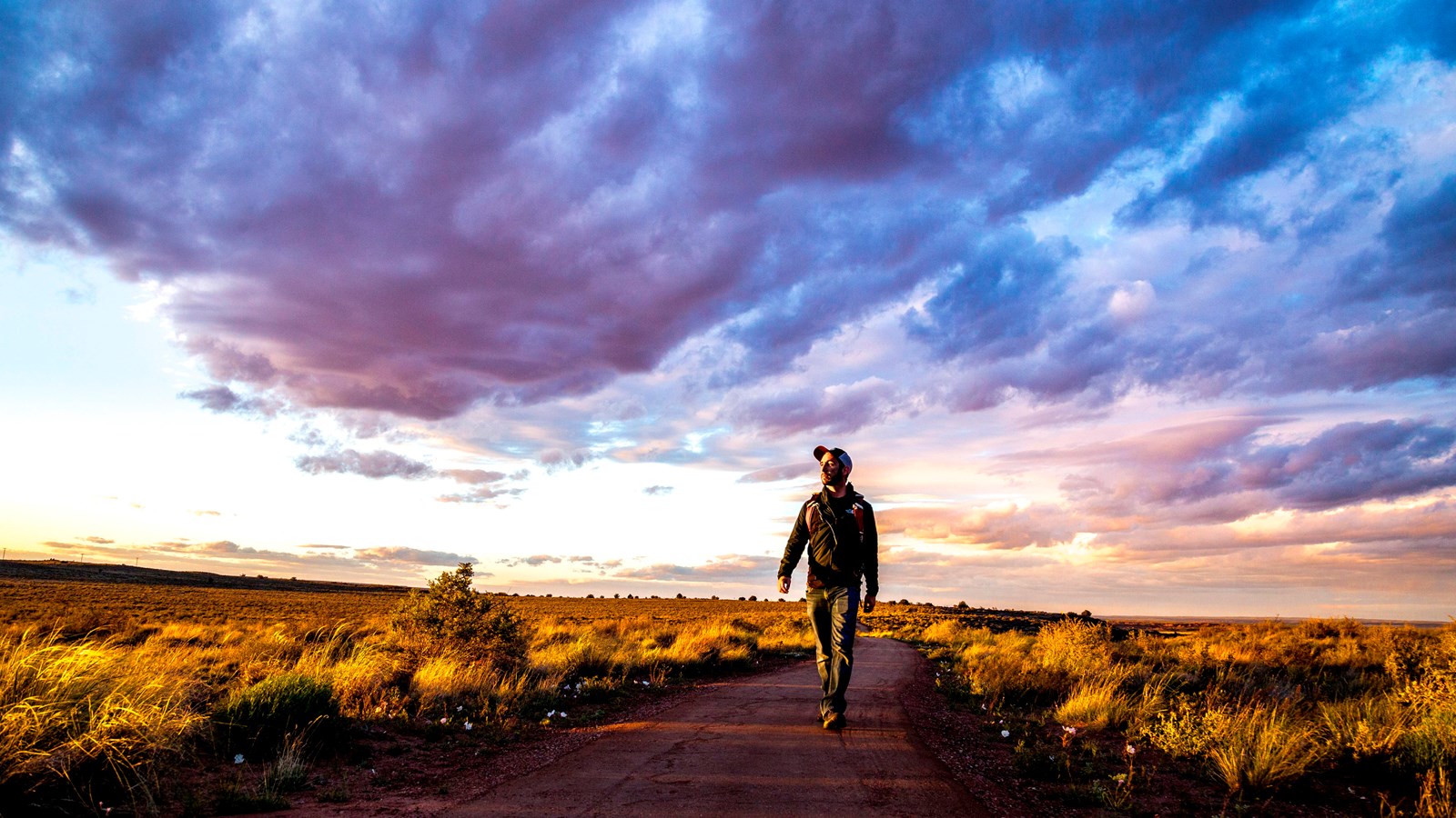 Hiker walking through the grassland under sunset clouds and sky.