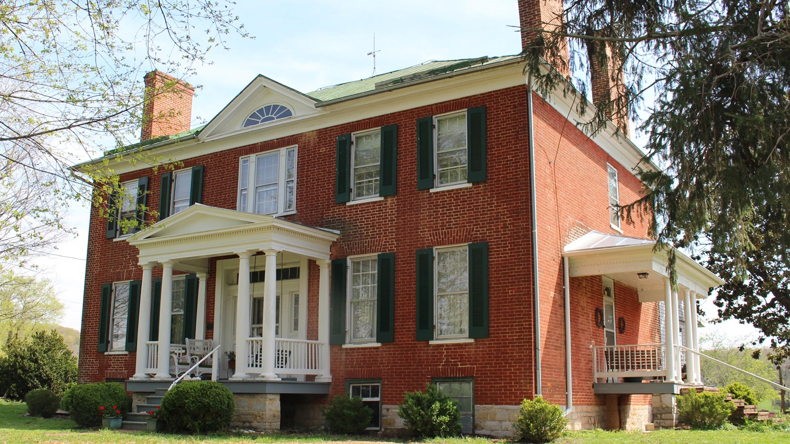 A Georgian style plantation house has a red brick façade, dark green shutters, and a white portico.