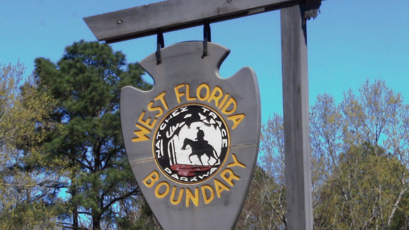 Wooden arrowhead shaped sign with yellow letters stating 