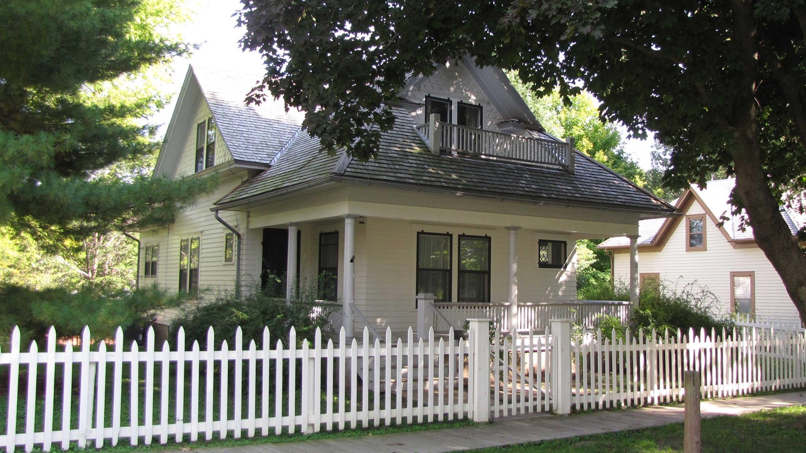 A picket fence encloses a white two-story house with a porch.