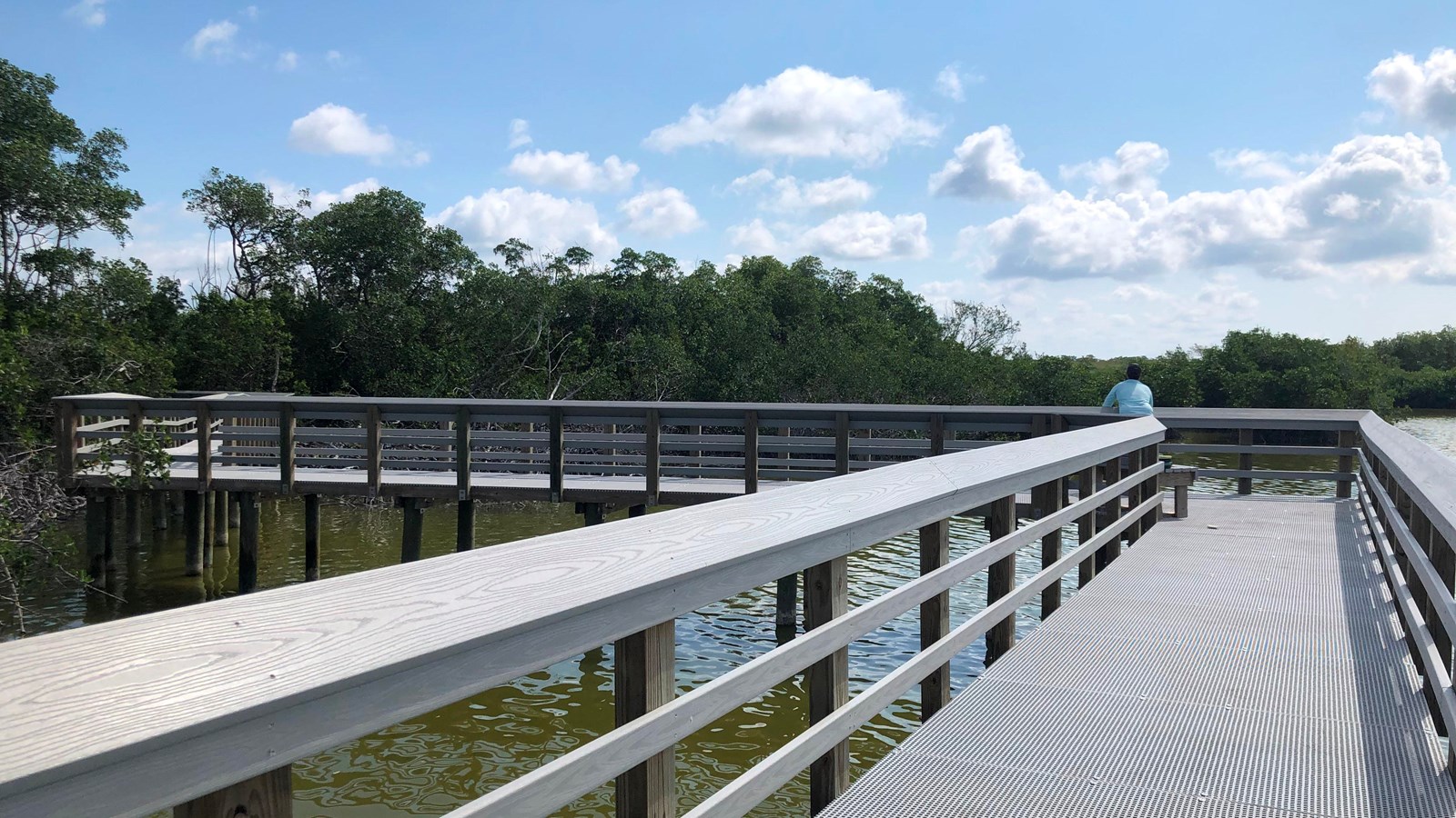 A gray composite boardwalk extends to the horizon. A man is fishing off the edge into the water