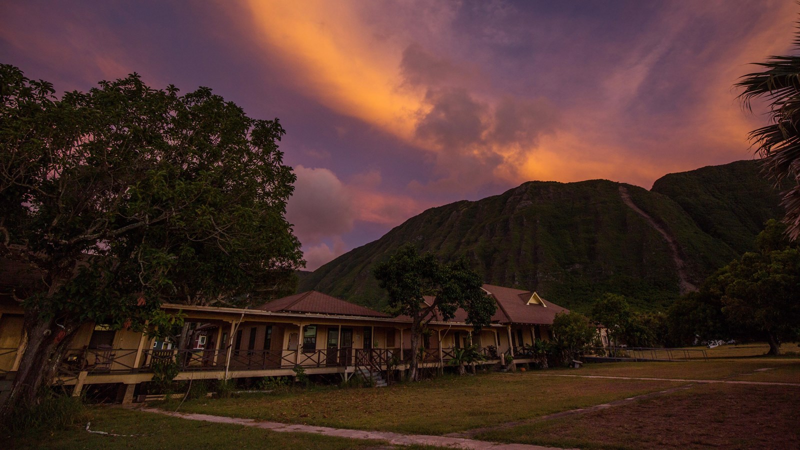 A vibrant and colorful sunset above a few buildings all connected by a covered walkway.