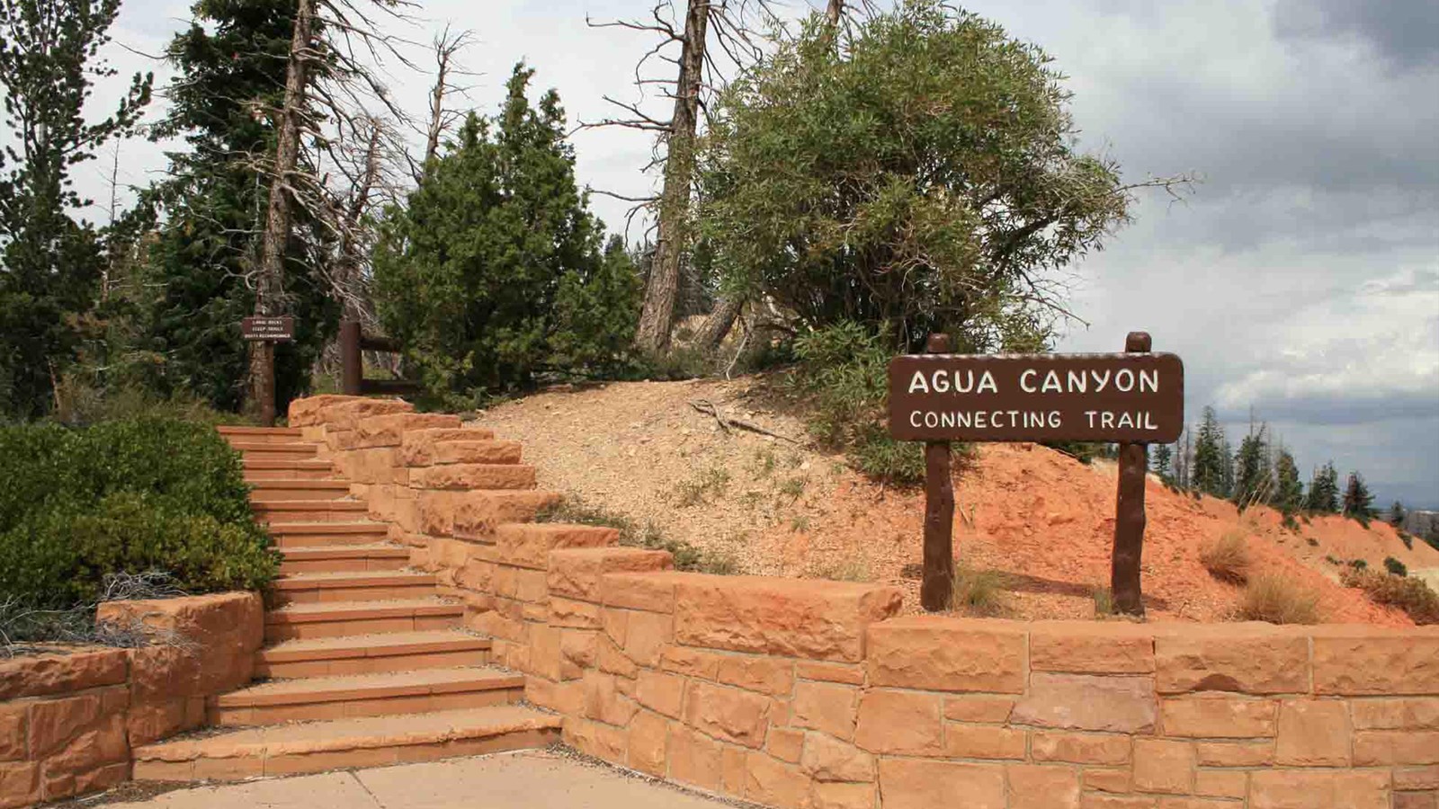 A sign reading Agua Canyon Connecting Trail leads up stairs to a forested cliff