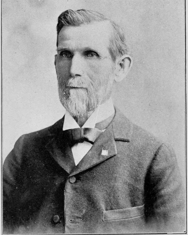 A black and white photograph of an older man with short hair and a goatee