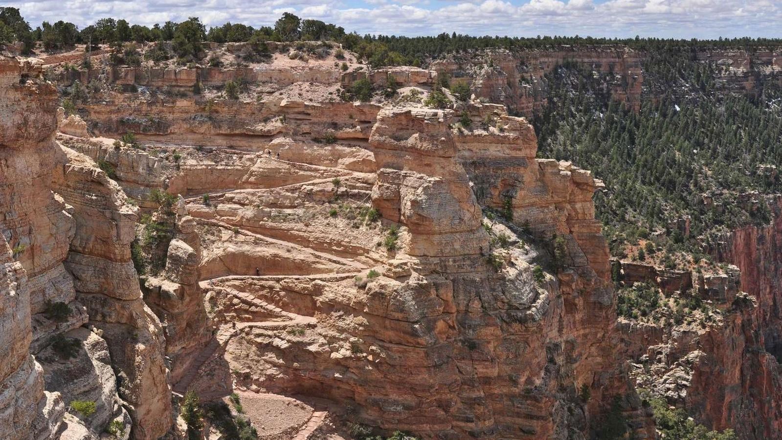 Several trail switchbacks are cut into a cliff of tan rock. 