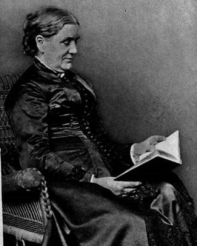 An older woman reads a book sitting in a chair