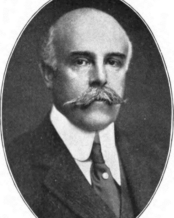 Black and white portrait of a white man with a mustache wearing jacket and tie