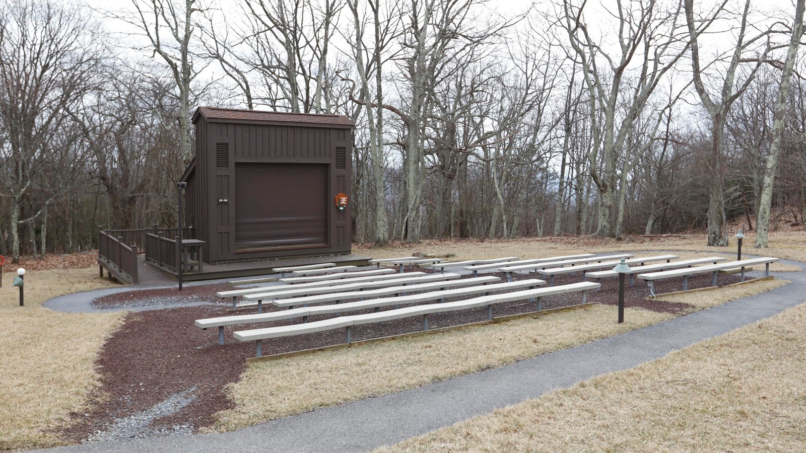 A color photograph of an amphitheater with benches facing a wood-paneled building.