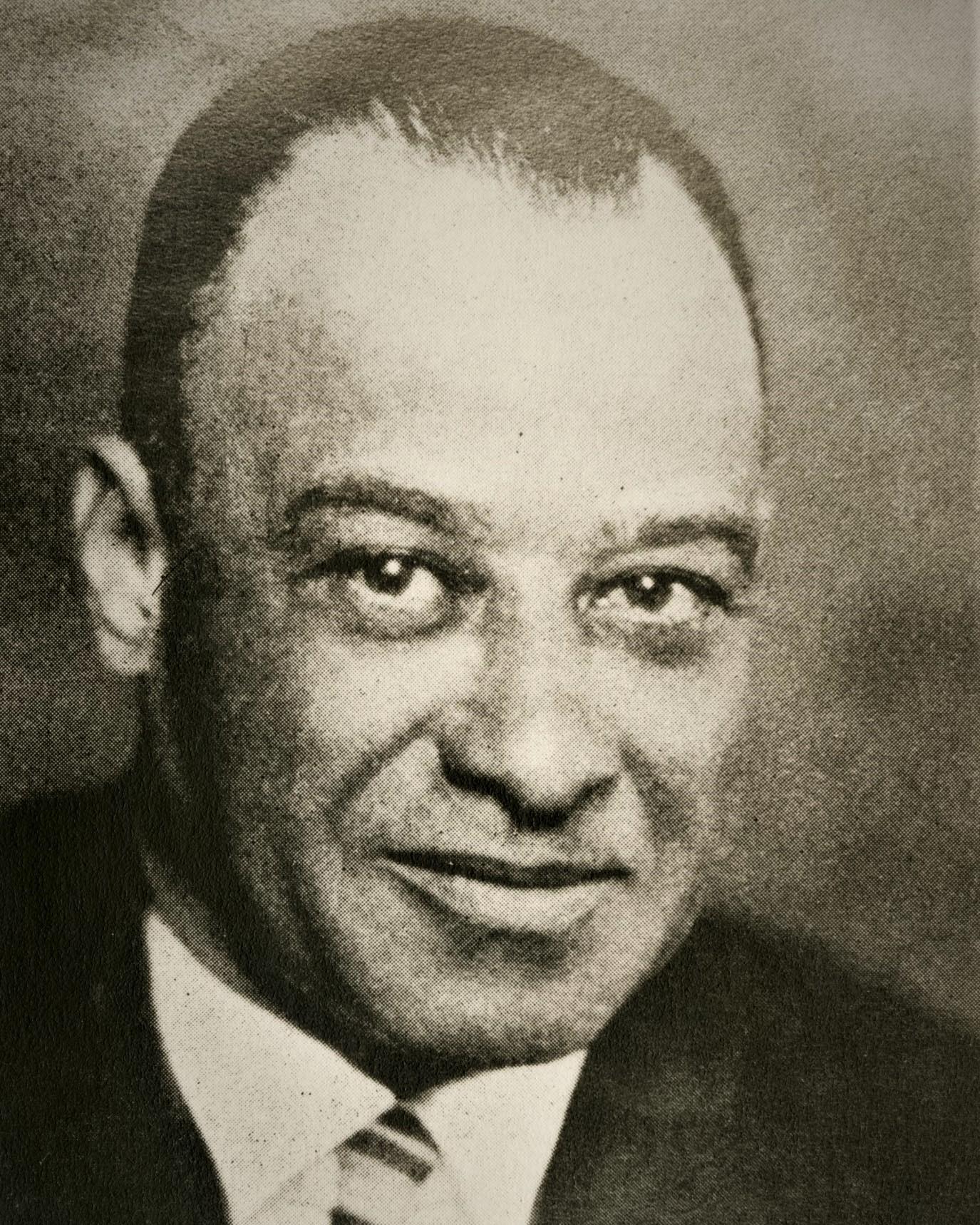 An African American man in dark jacket and tie.