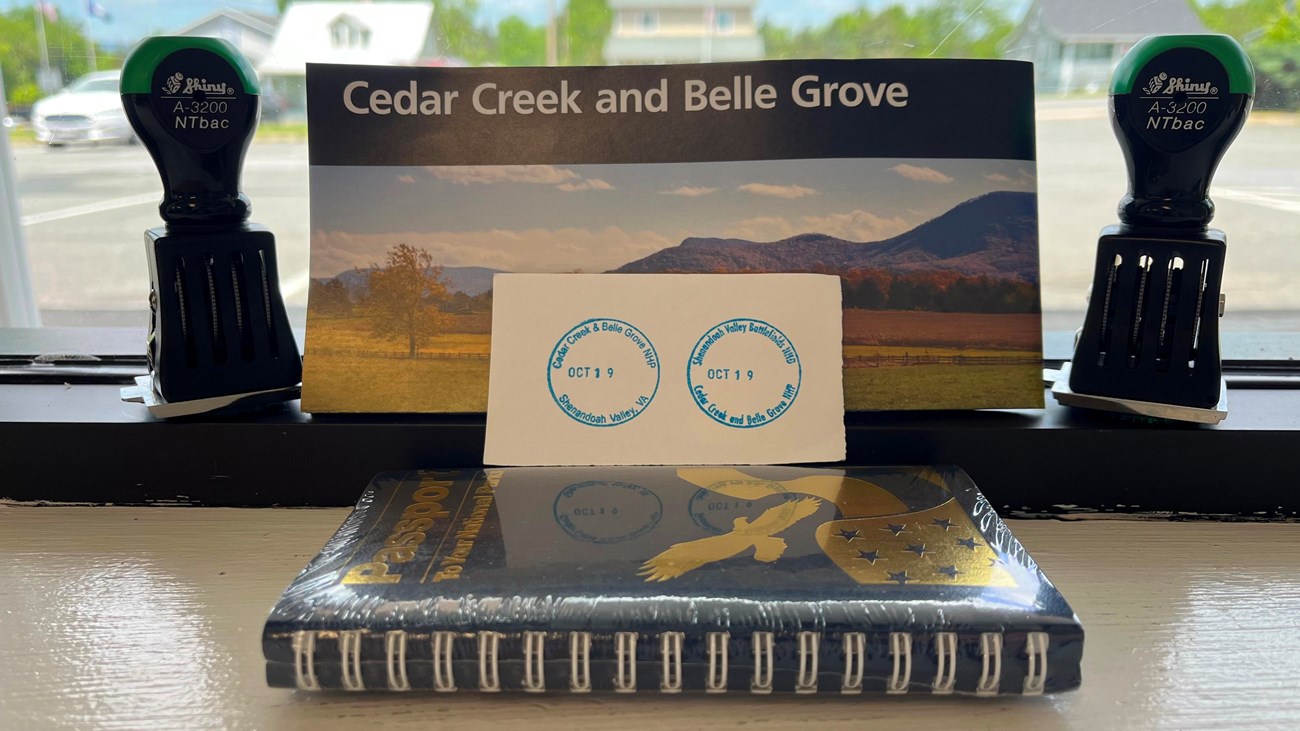 Two NPS cancellation stamps on a piece of paper propped up against a passport book and park map.