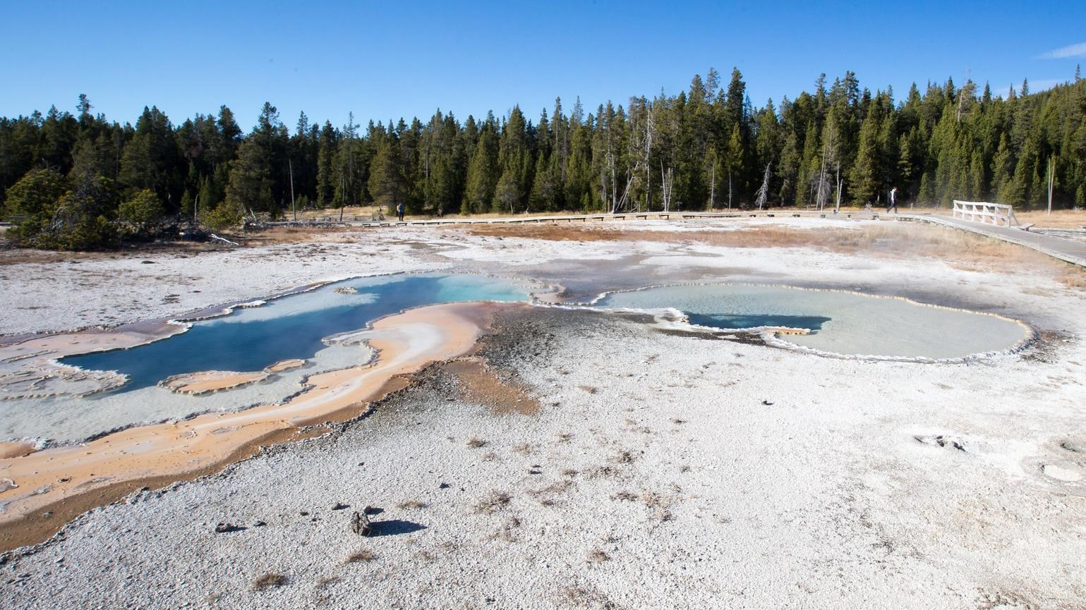 A hot spring with white sinter around the edges sits in a hydrothermal basin.