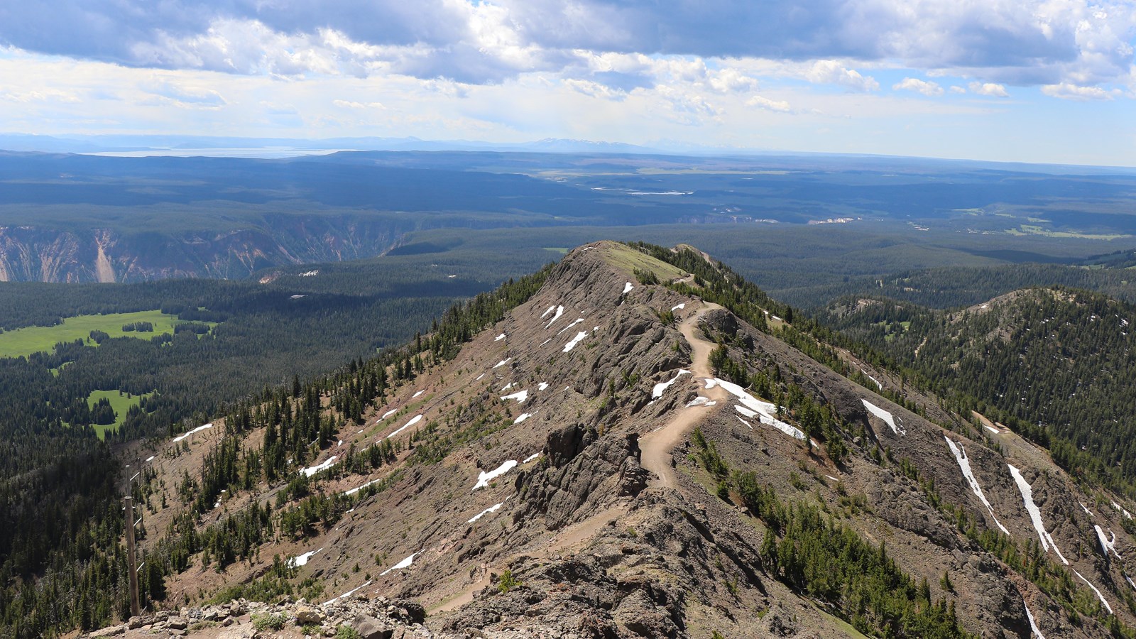 A trail crosses a ridgeline above forests and meadows.