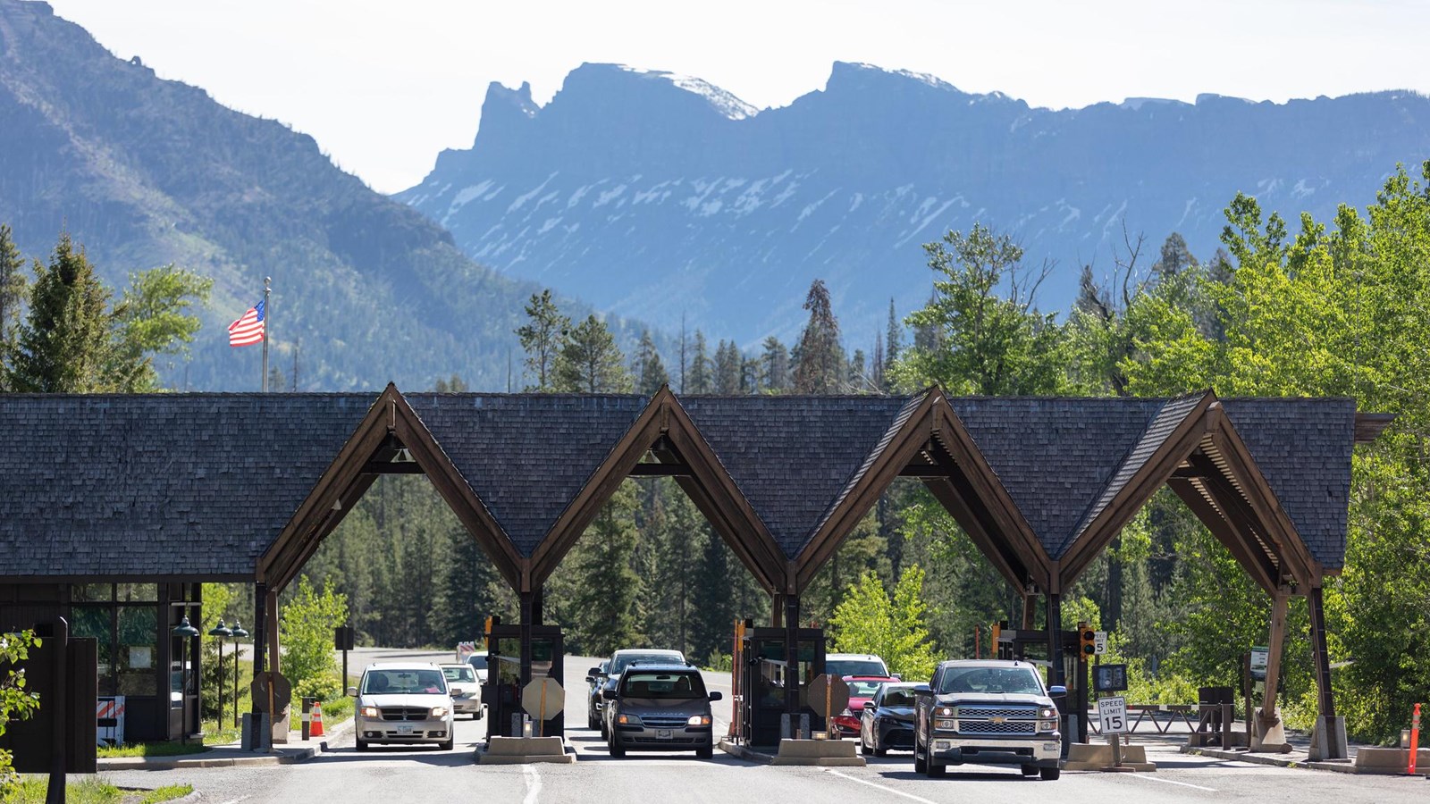 Vehicles travel through an entrance station with mountains in the distance.