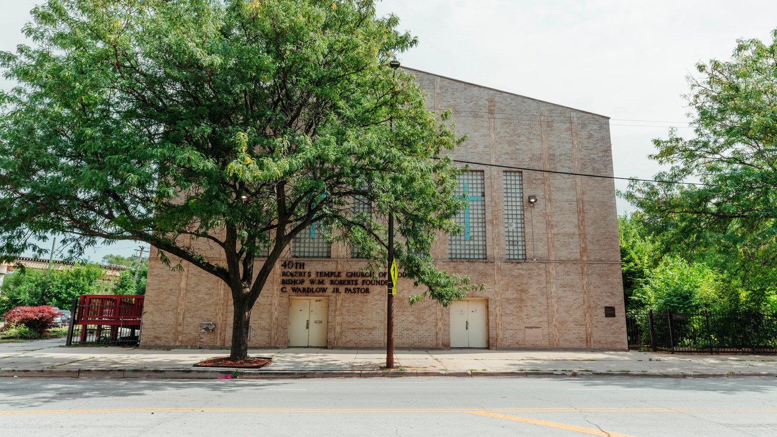 A multi-story tan brick church along a road. A tree stands in front.