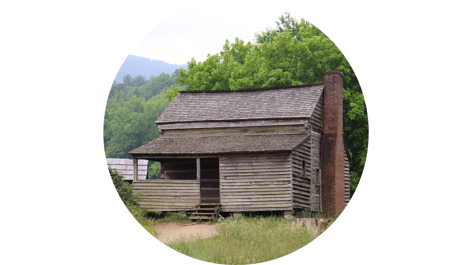 A home showing both log and frame construction with a brick chimney and a barn in the background.