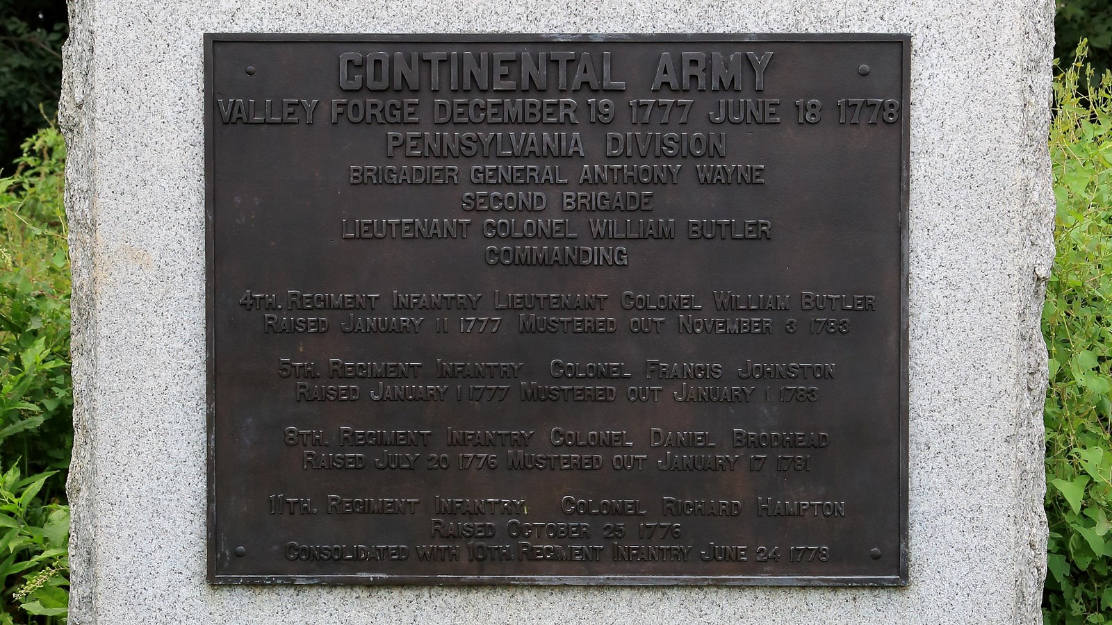 A large, smoothed granite block with a bronze plaque, sides and bottom rough.