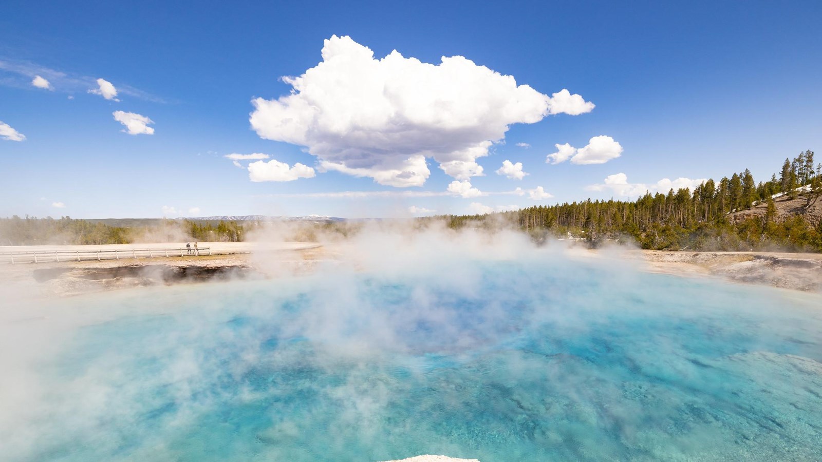 Steam rises off of a large, blue hot spring.