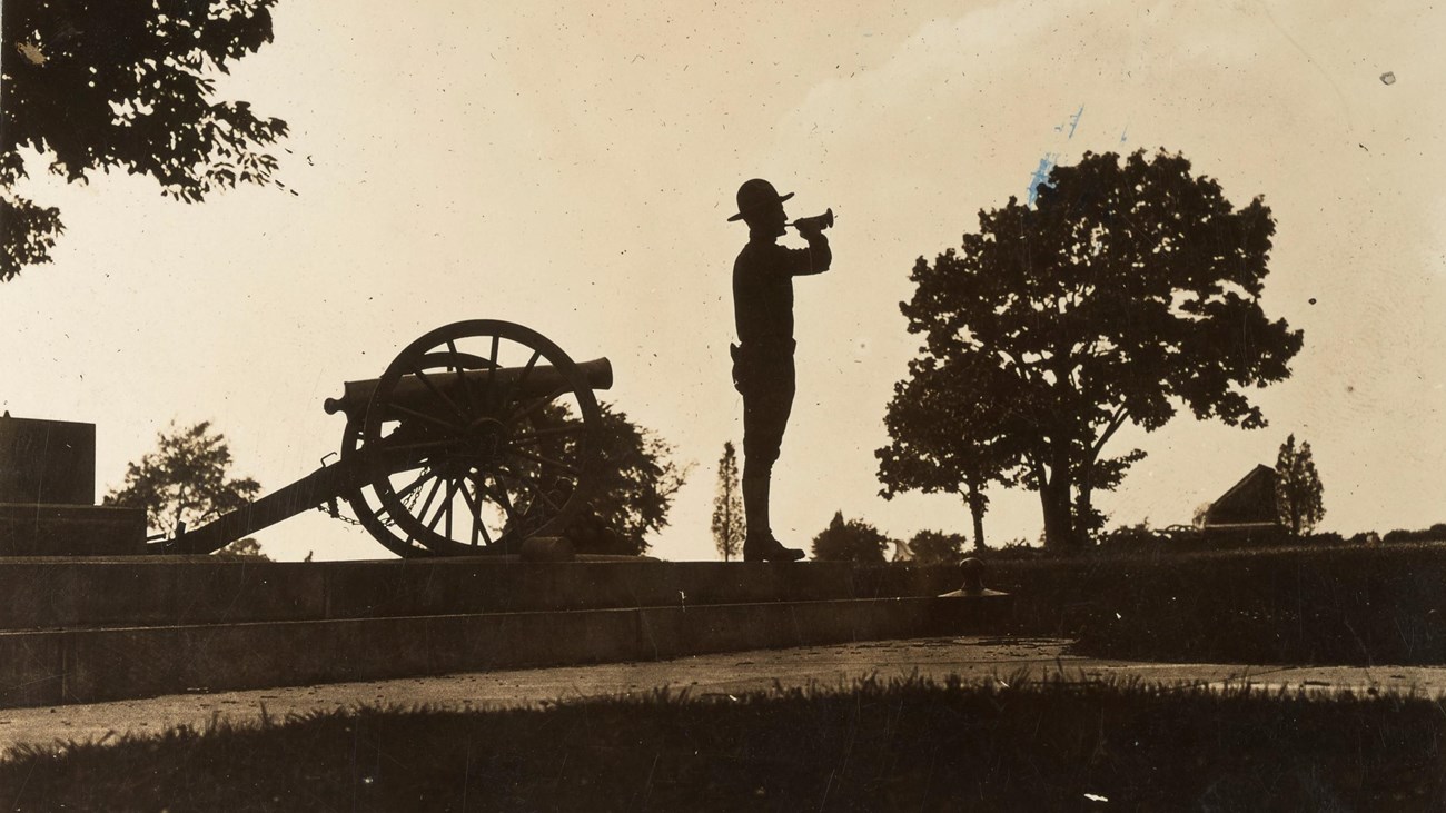 A black and white photograph showing the silhouette of lone bugler at Camp Colt