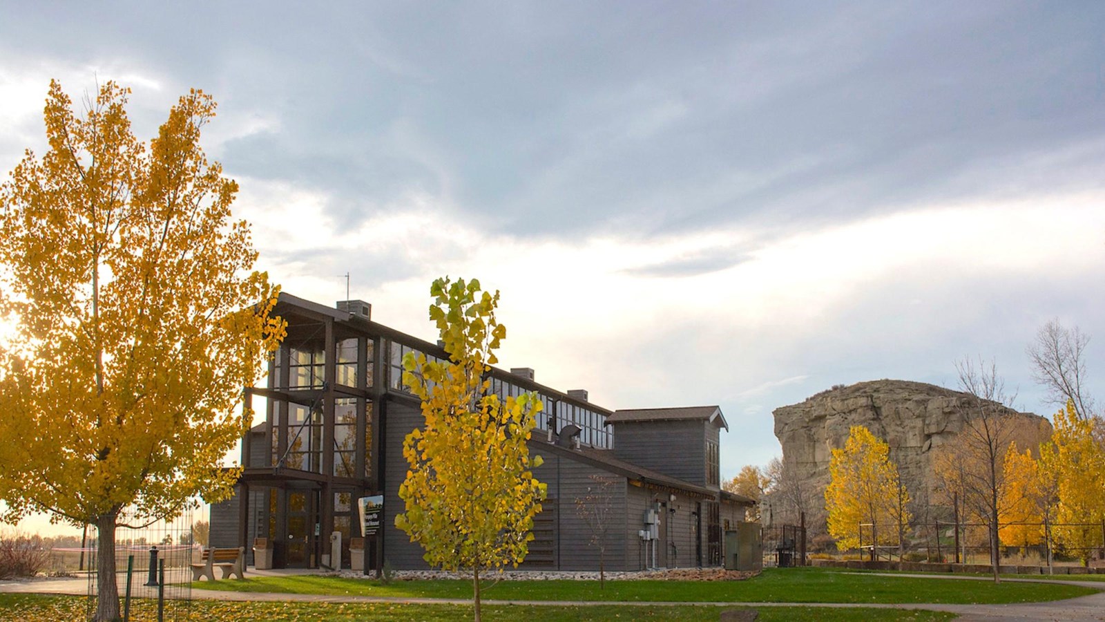 In the foreground, a modern two-story visitor center, surrounded with a grassy yard