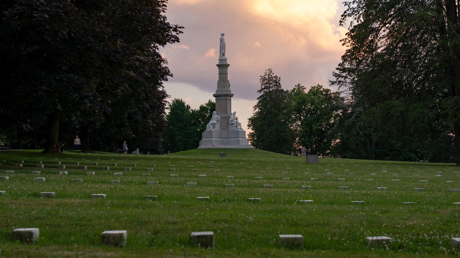 Rows of small headstones leading to a tall, narrow monument. 