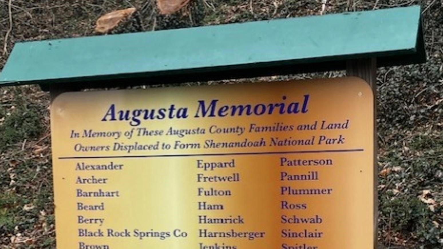 A golden sign with a green roof-structure lists the last names of former residents of the Park.