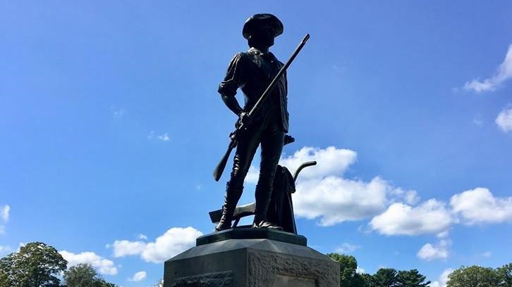 Statue of man in colonial clothing with a musket and plow set atop a granite pedestal